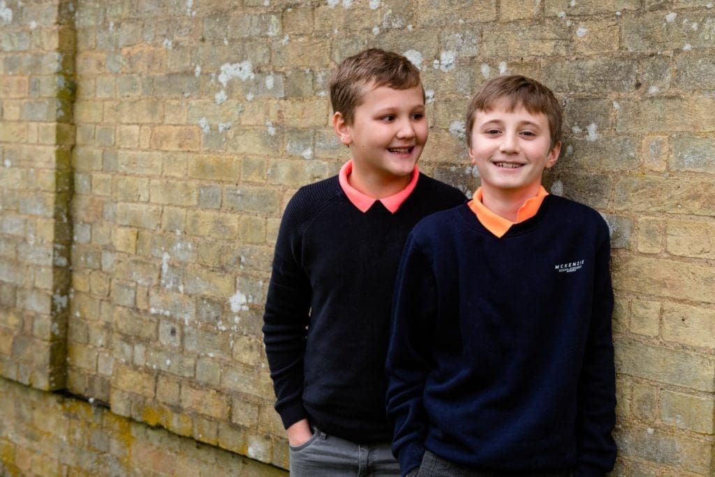 Families Portfolio - two young brothers are laughing together in matching outfits, leaning against a brick wall