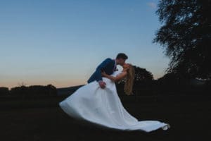 A bride and groom against a dusk sky, the groom is leaning the bride back in his arms for a romantic kiss - Bedfordshire Wedding Photographer