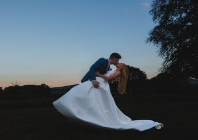 A bride and groom against a dusk sky, the groom is leaning the bride back in his arms for a romantic kiss - Bedfordshire Wedding Photographer