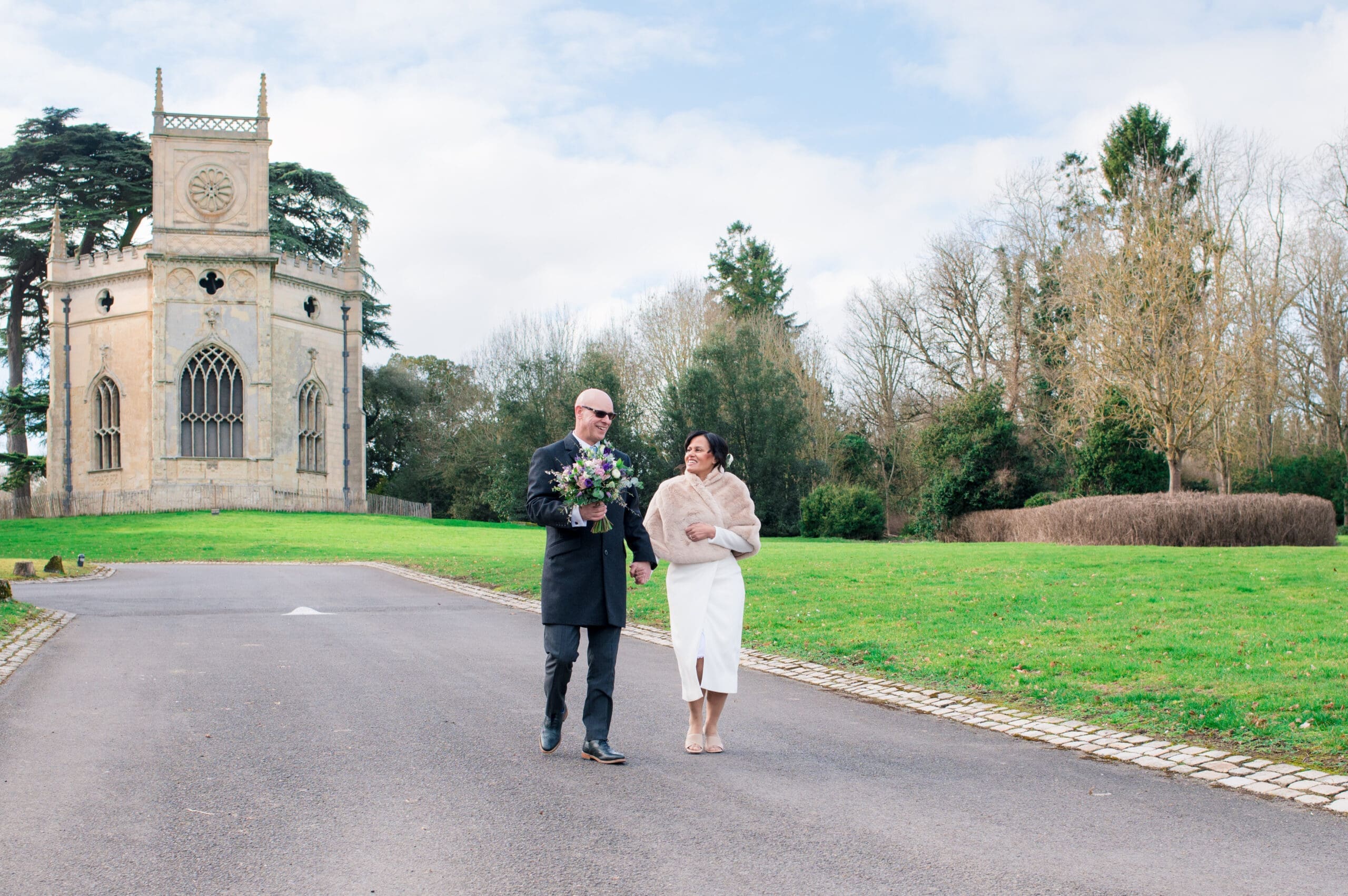 Just married couple walking down a slight hill with an old church in the background