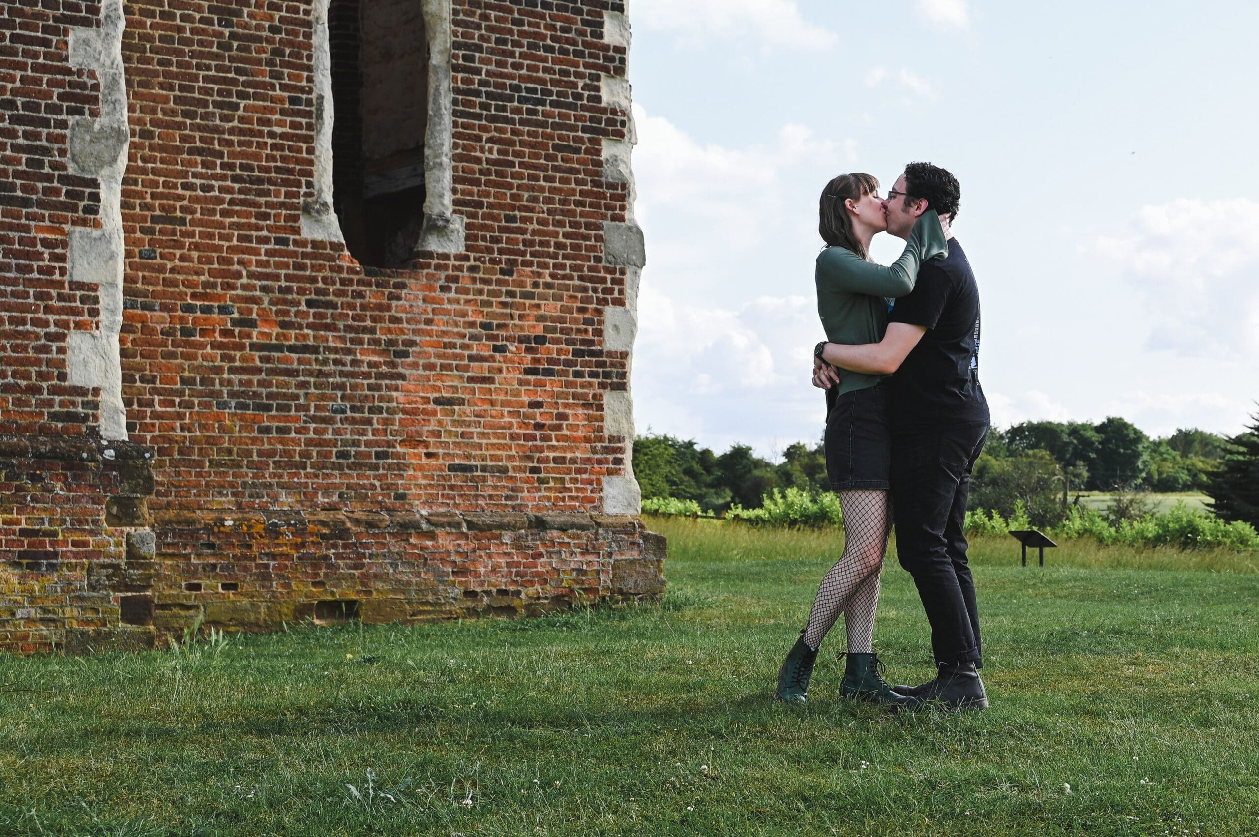 Engagement Photography Prices - A couple kiss and embrace outside an old red bricked manor house